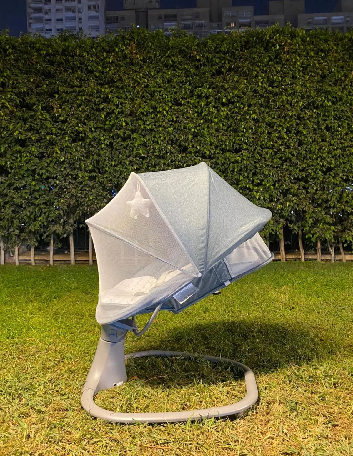 Baby swing with canopy on grass against a hedge background