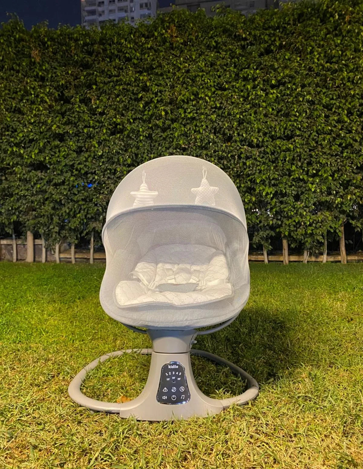Baby swing on grass with green hedge in the background