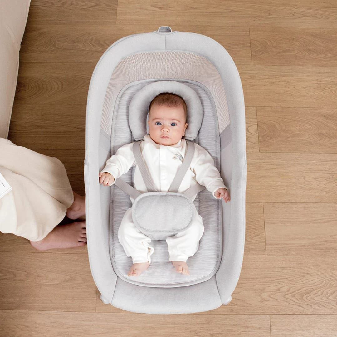 Baby in a gray baby seat on a wooden floor mastela x