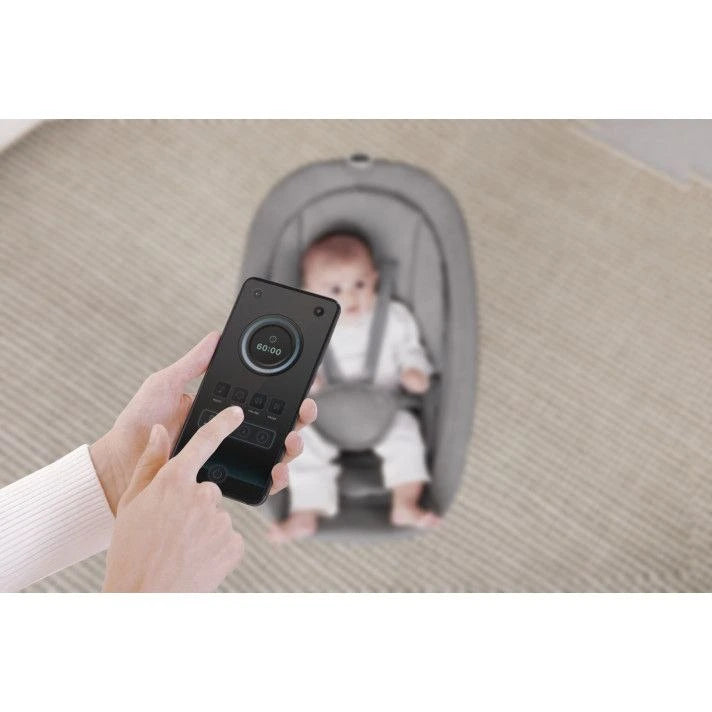 Person using a smartphone app to monitor a baby in a car seat on a carpeted floor.