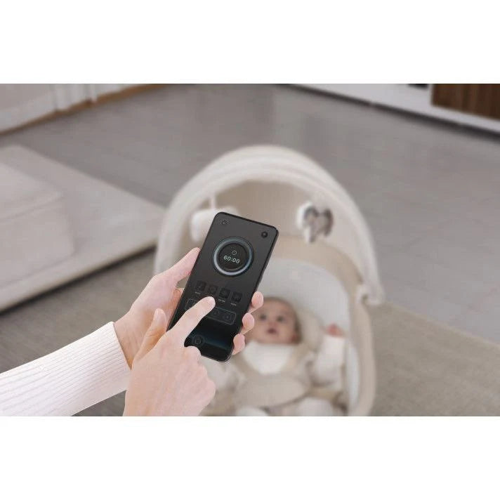 Person holding a baby monitor device with a baby in a crib in the سرير ماستيلا الهزازيعمل بابلكيشن علي الموبايل و سرعات هز مختلفه و تايمرbackground